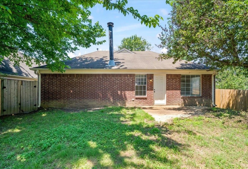 Rear brick exterior featuring a white entry door, multiple windows, and an exposed chimney