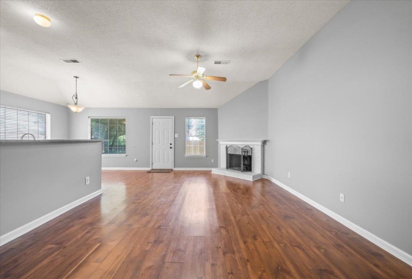 Spacious living area featuring wood-finish flooring, a corner fireplace with a white mantel, and a ceiling fan