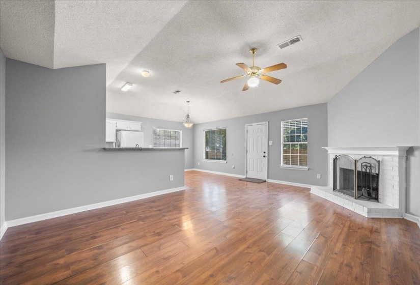 Spacious living area featuring wood-finish flooring, a white brick fireplace, and vaulted ceilings