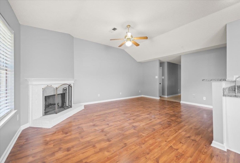 Spacious living area featuring wood-finish flooring, a white brick fireplace with mantel, and a ceiling fan