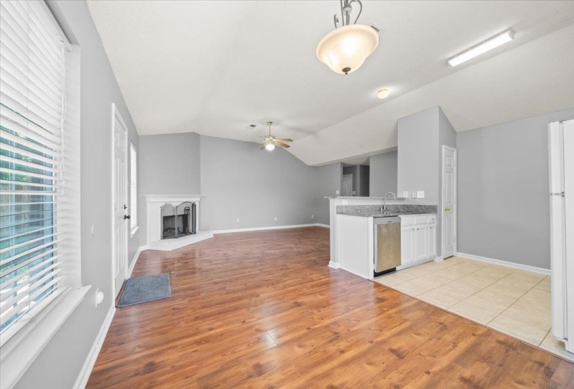 Open-concept living space featuring vaulted ceilings, wood-finish flooring, a corner fireplace, and a kitchen island with stone countertops and an integrated sink