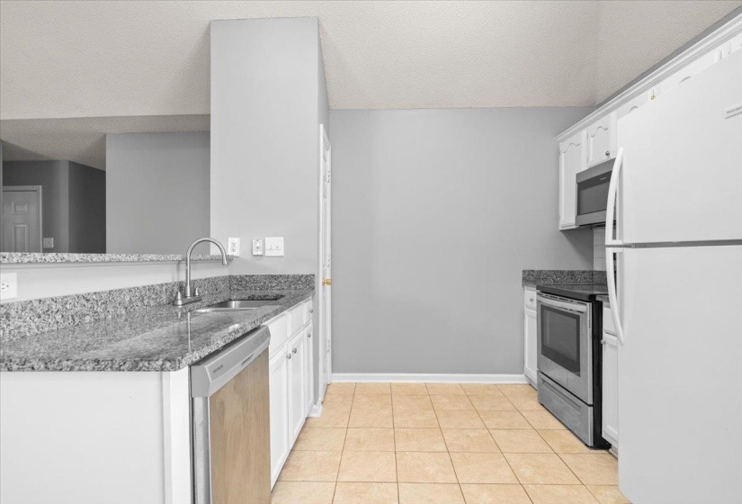 Kitchen featuring granite countertops, white cabinetry, a double-basin stainless steel sink with a gooseneck faucet, and a full suite of appliances including a stainless steel dishwasher, built-in microwave, and range