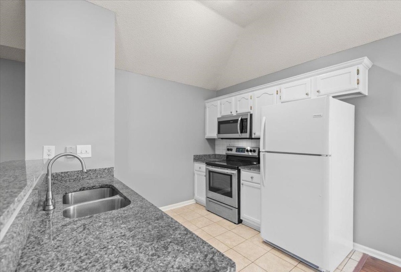 Kitchen featuring granite-style countertops, stainless steel double basin sink with gooseneck faucet, white cabinetry, stainless steel microwave, and a white refrigerator