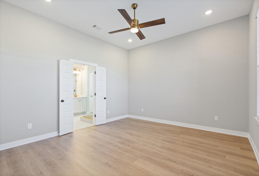 Spacious room featuring vaulted ceilings, recessed lighting, wood-finish flooring, a ceiling fan with integrated light, and double doors opening to a bathroom with a glass-enclosed shower