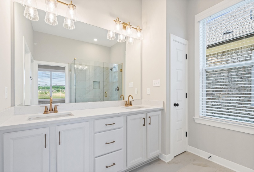 Bathroom featuring a dual vanity with white cabinetry, light-toned countertops, and gold-finish fixtures