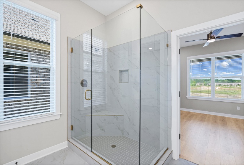 Walk-in shower featuring clear glass enclosure with gold-toned hardware, white marble-look tile walls, a built-in niche, and a tiled shower bench