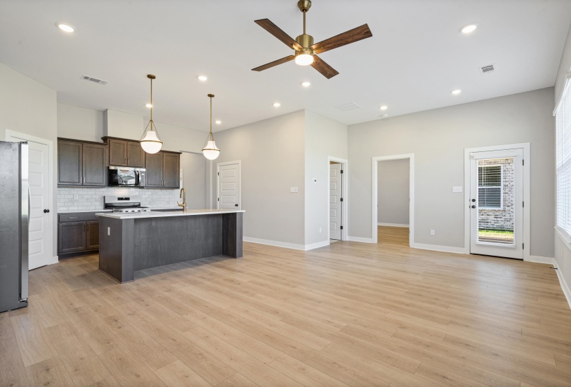 Open-concept living space featuring a kitchen with dark cabinetry, stainless steel appliances, a center island with pendant lighting, and light wood-finish flooring throughout