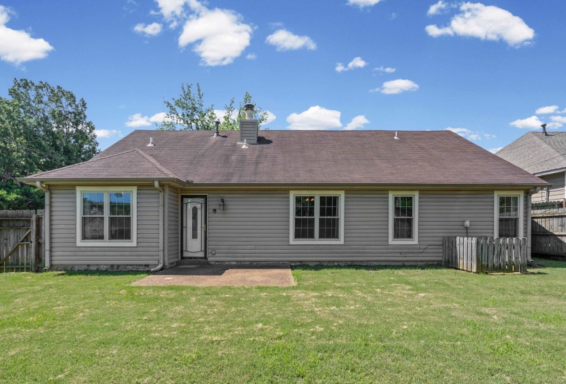 Rear exterior featuring siding, multiple windows, a rear entry door with a divided light insert, a concrete patio, and a grass lawn