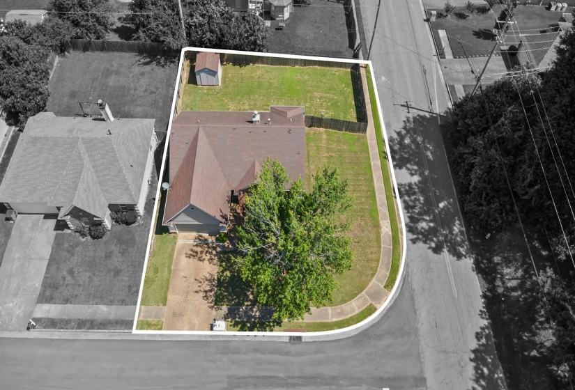 Corner lot property with mature trees, a driveway, and an additional storage shed