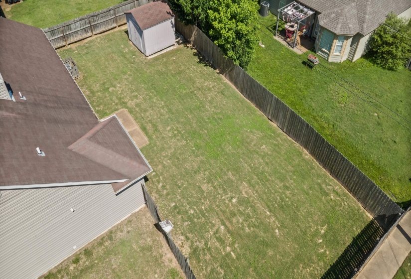 Expansive lawn area featuring a privacy fence, an exterior storage shed, and a section of the main residence with a brown shingle roof and light-colored siding