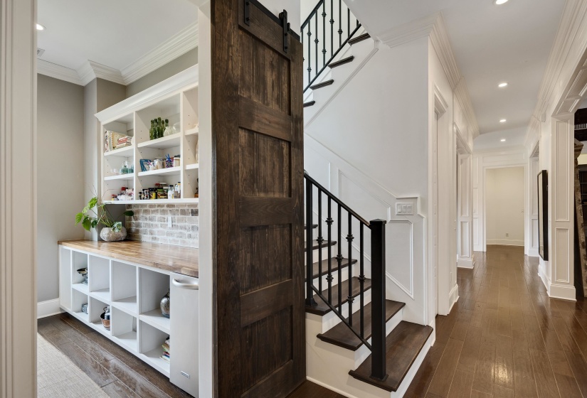 Architectural details featuring a dark wood-finish barn door, white wainscoting, and a staircase with dark wood-finish treads and black metal balusters