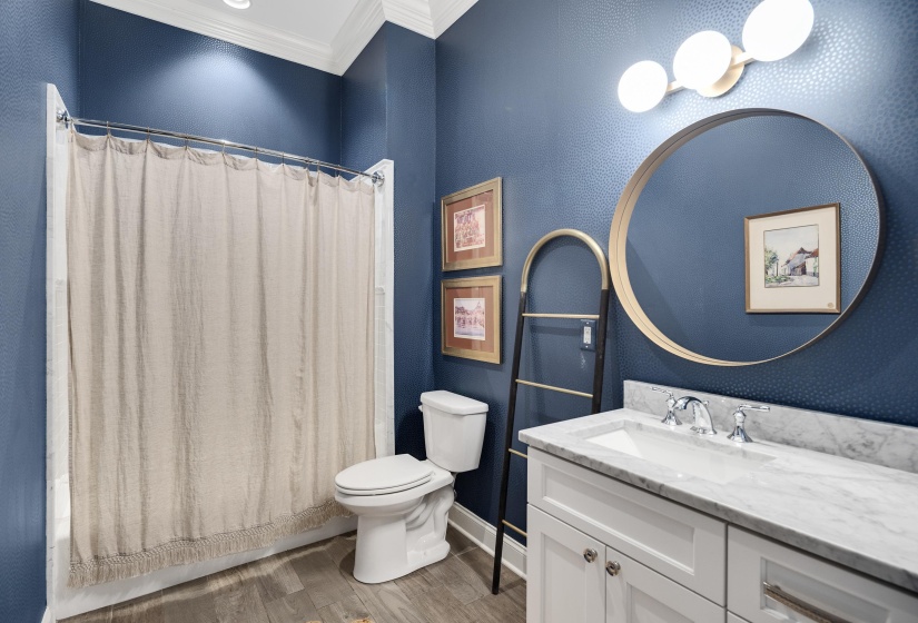 Bathroom featuring wood-finish flooring, a white vanity with a stone countertop, and a circular mirror with a gold-tone frame