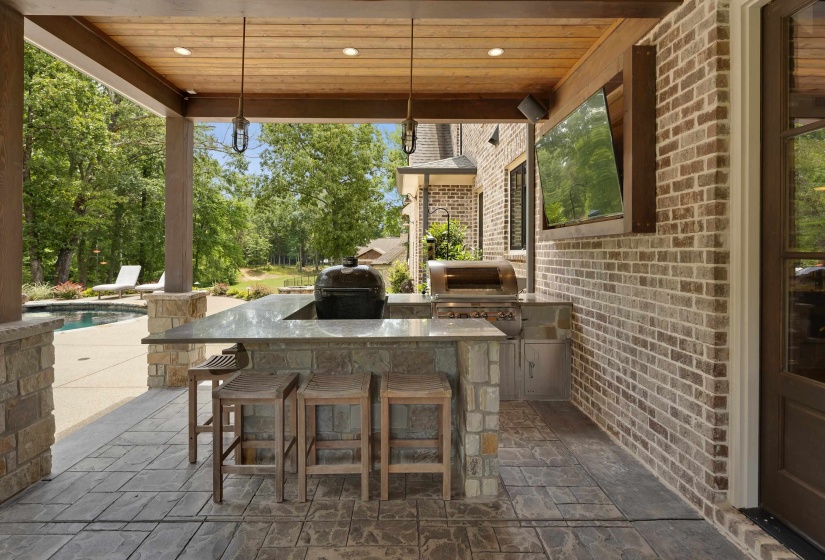 Covered outdoor kitchen featuring a built-in grill, stone-clad island with a countertop, recessed lighting, and a mounted screen