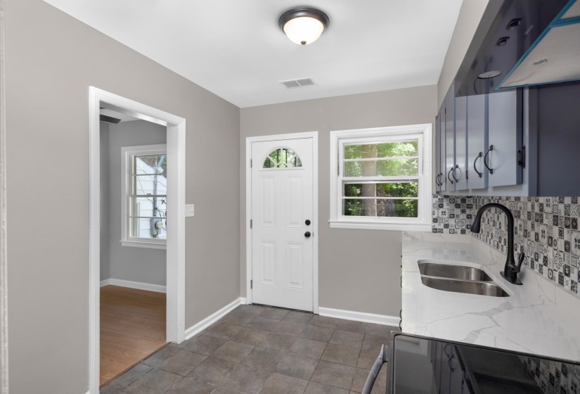 Kitchen featuring gray cabinetry, white countertops, dual basin stainless steel sink with a matte black faucet, and a patterned tile backsplash