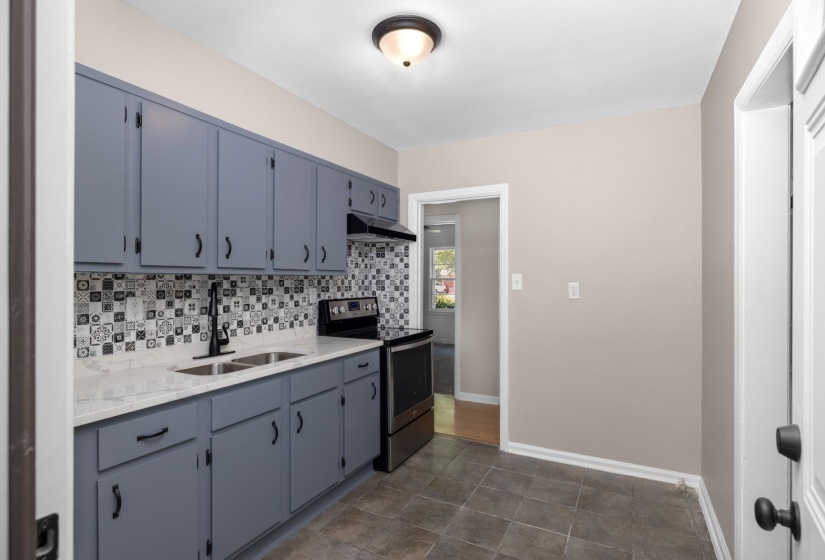 Kitchen featuring slate-finish tile flooring, painted cabinetry, patterned tile backsplash, light-toned countertops, and a black range with coordinating hood