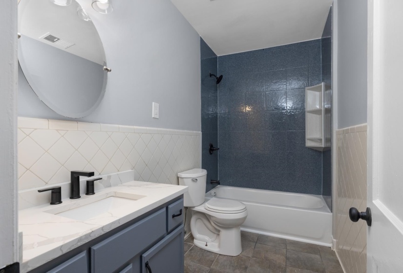 Bathroom featuring a white bathtub, blue tiled shower surround, built-in shower shelving, and a vanity with a white countertop