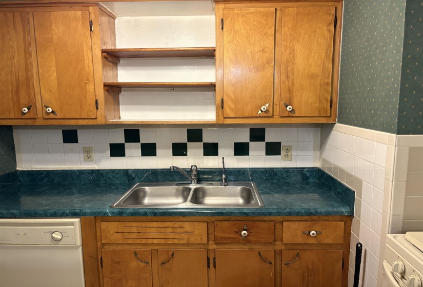 Kitchen featuring open shelves, white dishwasher, brown cabinets, tasteful backsplash, and dark countertops