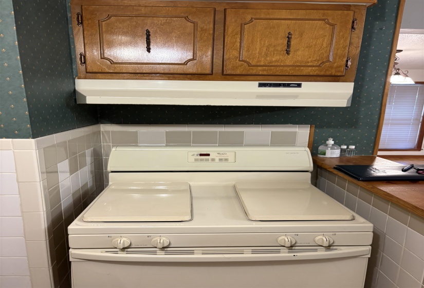 Kitchen view of wallpapered walls, ventilation hood, white range oven, and brown cabinetry