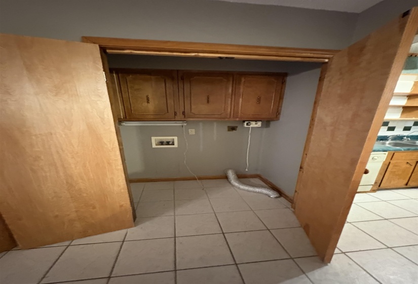 Washroom with hookup for a washing machine, light tile patterned floors, cabinet space, and hookup for an electric dryer