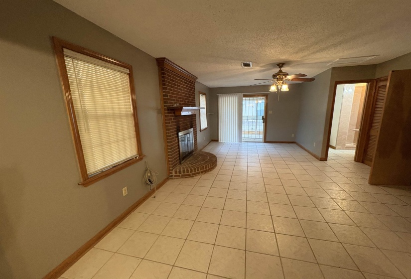 Den with light tile patterned floors, a textured ceiling, a fireplace, and ceiling fan
