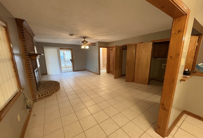 Den featuring a textured ceiling, a brick fireplace, light tile patterned floors, and ceiling fan