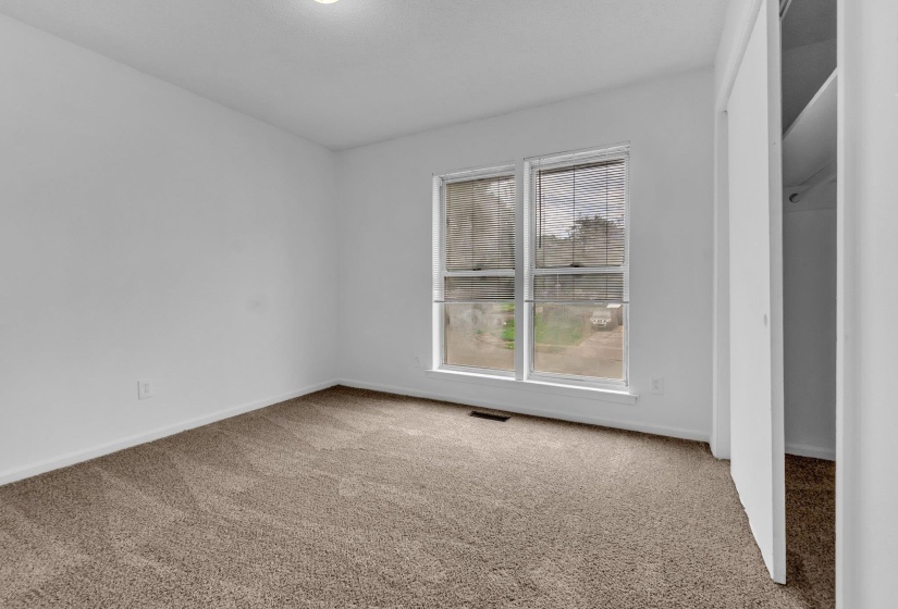 Neutral-toned carpeting paired with white walls, featuring a double window with blinds and a built-in closet with shelving
