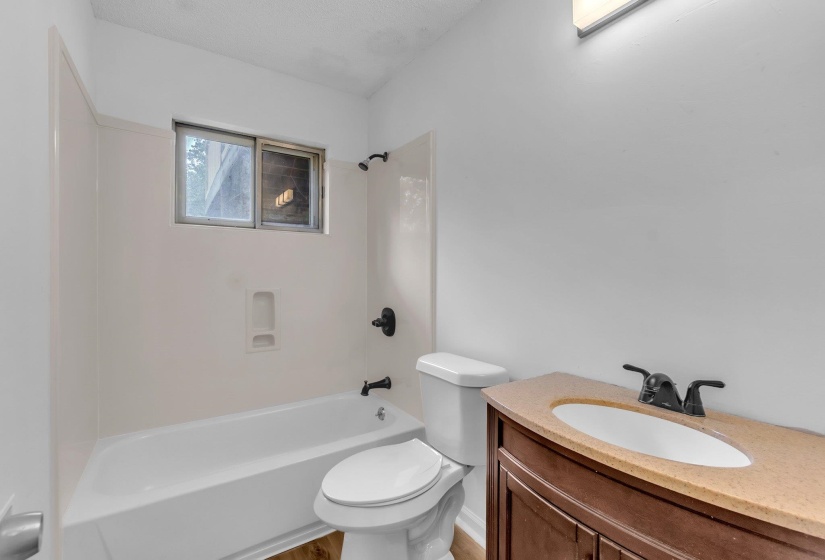 Bathroom featuring a white bathtub with dark fixtures, a window above the tub, a white toilet, and a wood-finish vanity with an integrated sink and dark faucet