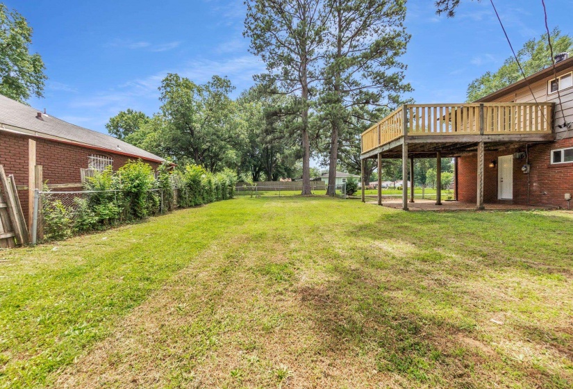 Expansive backyard featuring a large wooden deck, mature trees, and a chain-link fence