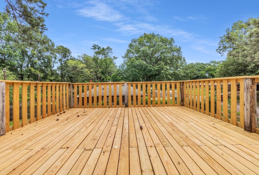 Spacious outdoor wood deck with natural wood railing, surrounded by mature trees and verdant foliage