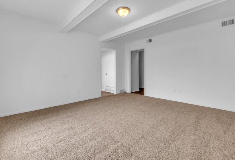 Spacious room featuring neutral carpeting, white walls, exposed ceiling beams, and a semi-flush mount light fixture