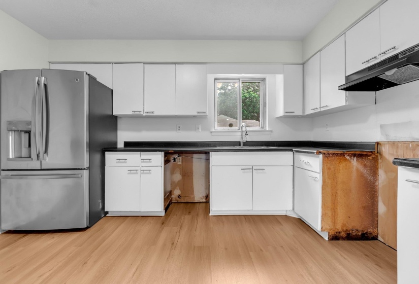 Kitchen featuring white upper and lower cabinetry, dark countertops, a stainless steel refrigerator, and wood-finish flooring