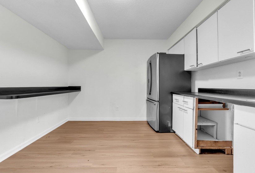 Kitchen area featuring wood-finish flooring, white cabinetry with silver-toned hardware, a stainless steel refrigerator, and dark countertops