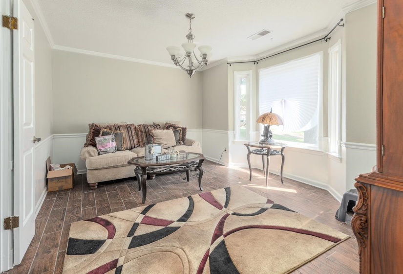 Living room with dark wood finished floors, crown molding, and a chandelier