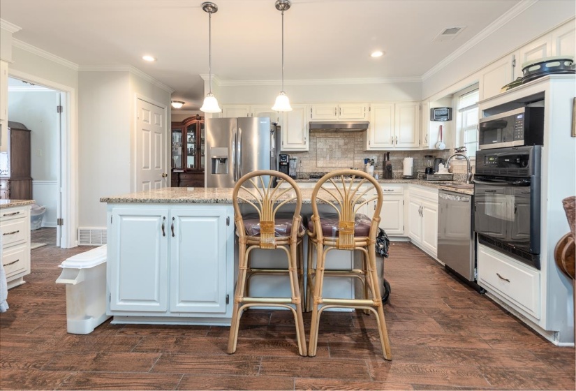 Kitchen featuring tasteful backsplash, white cabinets, hanging light fixtures, light stone countertops, and a kitchen island