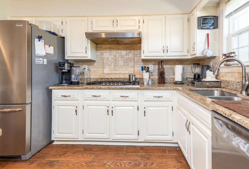 Kitchen with stainless steel appliances, backsplash, light stone countertops, and white cabinetry