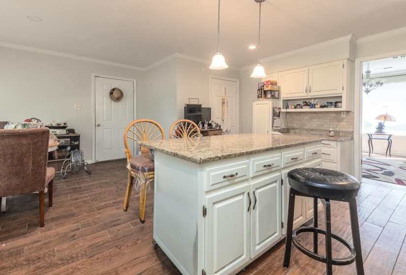 Kitchen with white cabinets, light stone counters, decorative light fixtures, dark wood-style floors, and crown molding