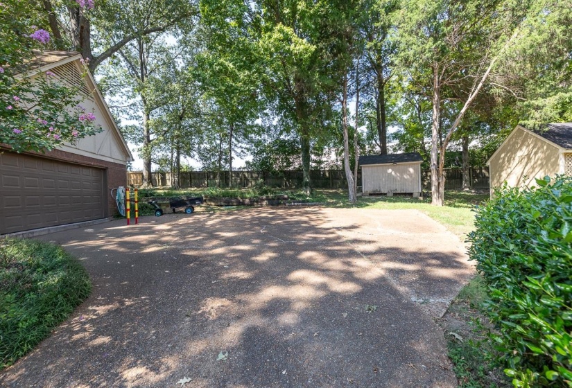 Fenced backyard with driveway, a storage unit, and a garage