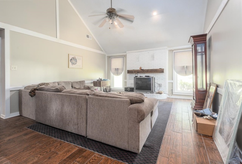 Living room featuring dark wood-style floors, a fireplace, a ceiling fan, and high vaulted ceiling