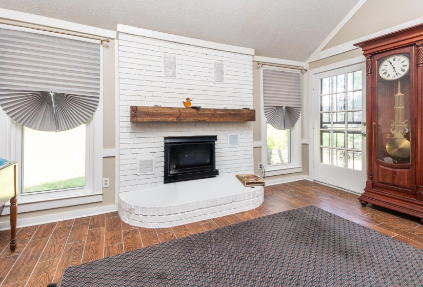Living room featuring wood finish floors, a brick fireplace, lofted ceiling, and a textured ceiling