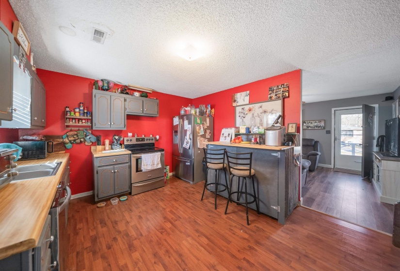 Kitchen with dark wood-style floors, light countertops, stainless steel appliances, gray cabinets, and a kitchen breakfast bar