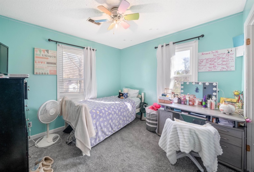 Carpeted bedroom with a ceiling fan, multiple windows, and a textured ceiling