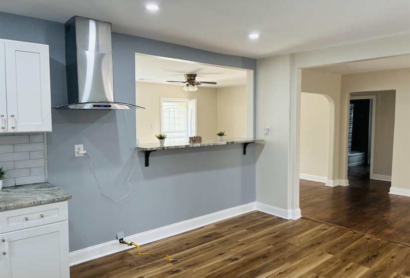 Kitchen with light stone countertops, a kitchen bar, white cabinetry, dark wood-style flooring, and decorative backsplash