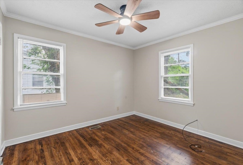 Room featuring a ceiling fan with integrated lighting, wood-finish flooring, two window openings, white baseboards, and crown molding