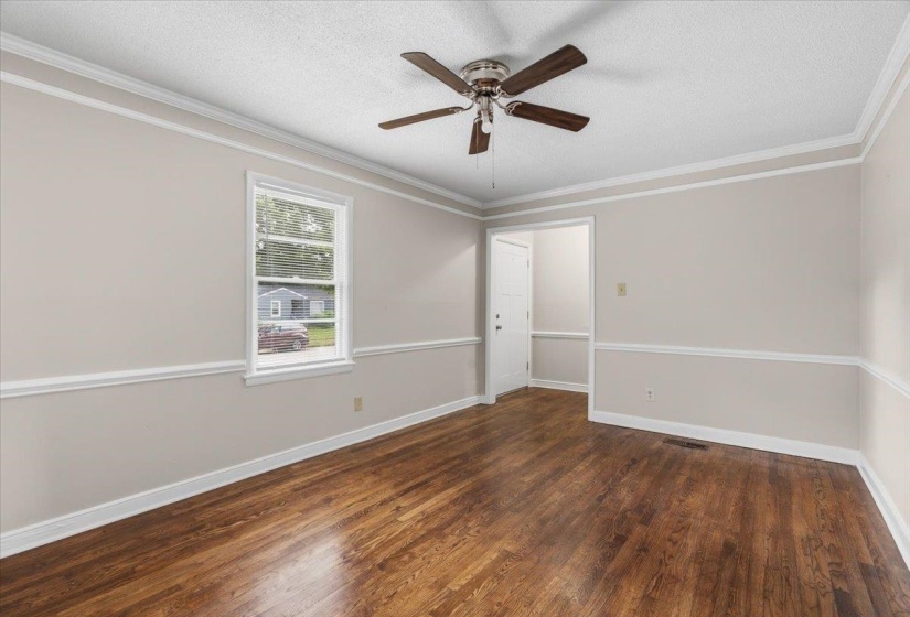 Spacious room featuring wood-finish flooring, light-toned walls with chair rail molding, and a ceiling fan with integrated lighting
