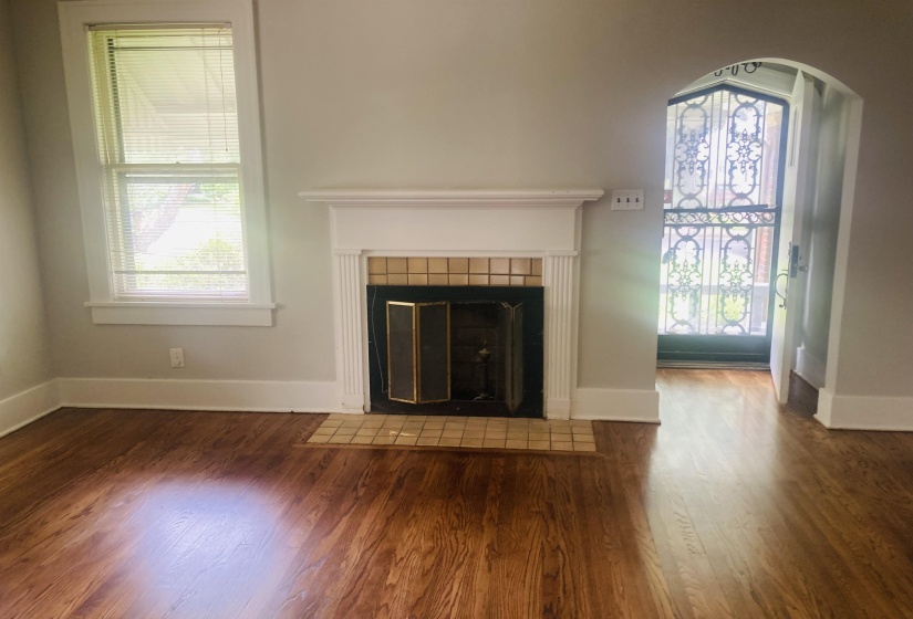 Living area featuring wood-finish flooring, a decorative fireplace with a tile hearth and surround, and an arched doorway leading to an ornate security door