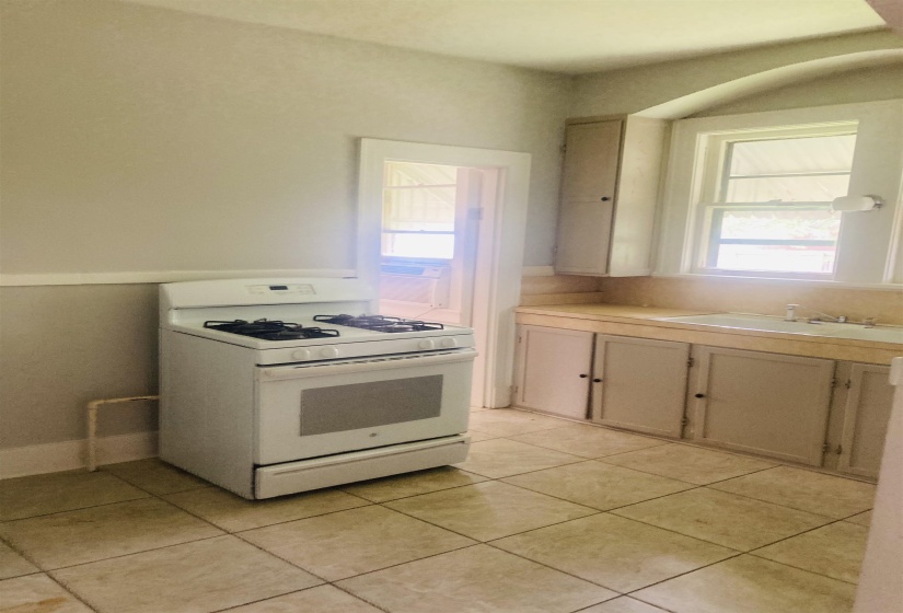 Kitchen featuring a white gas range, tiled flooring, built-in cabinetry, and a window with an arched alcove