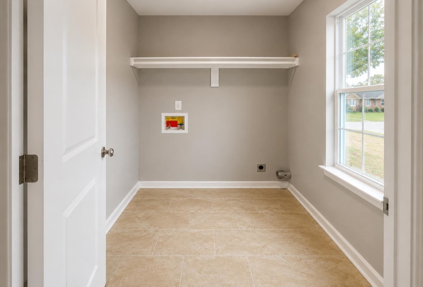 Laundry area featuring beige tile flooring, light gray walls, a white sash window, and a built-in white shelf