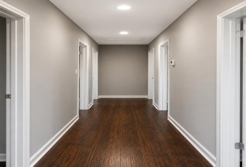 Hallway featuring wood-finish flooring, light gray wall paint, white trim, recessed lighting, and multiple paneled doors