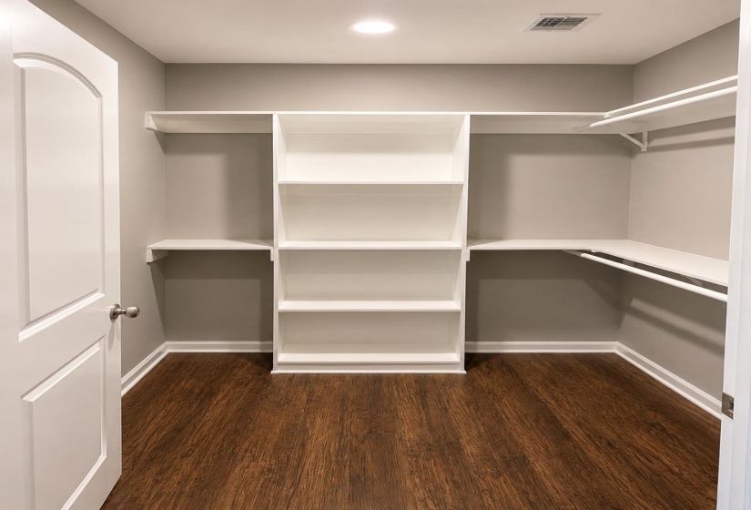 Walk-in closet featuring built-in white shelving and hanging rods, wood-finish flooring, recessed lighting, and light gray wall paint