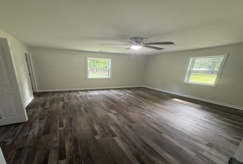 Spacious room featuring wood-finish flooring, two windows with exterior views, a ceiling fan with integrated lighting, and white baseboards
